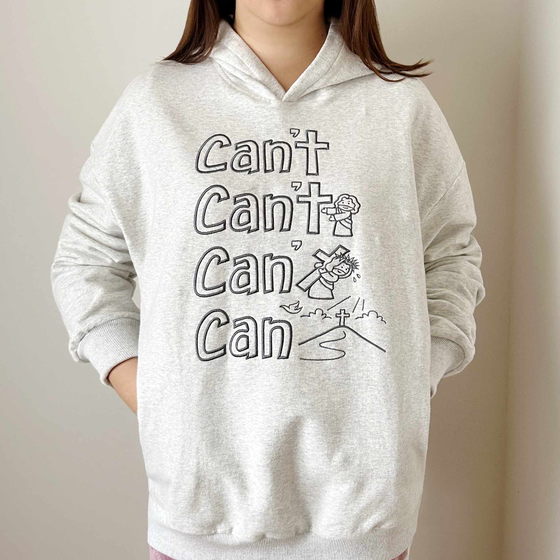 model wearing heather grey hoodie with embroidered message oj jesus carrying the cross making the word can't into can